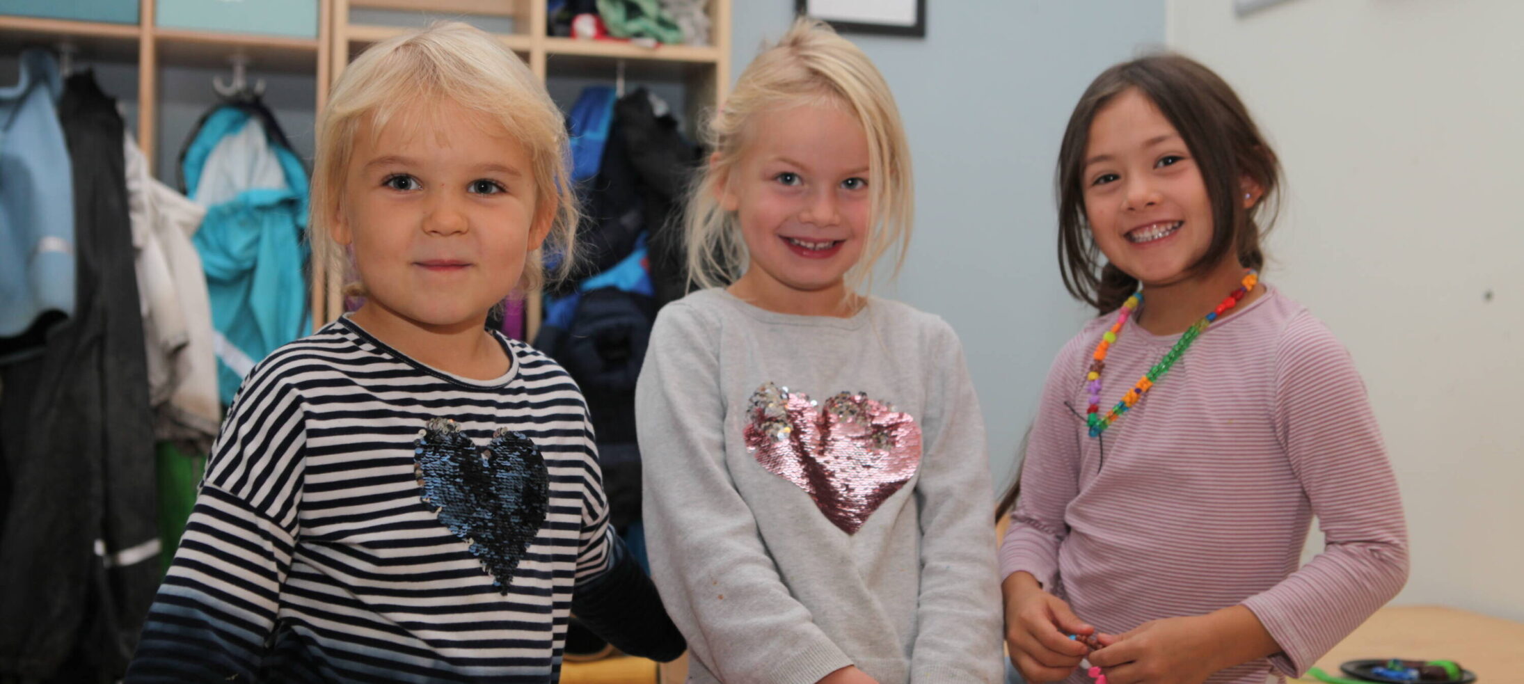 Tre små flickor poserar i kapprummet på förskolan.