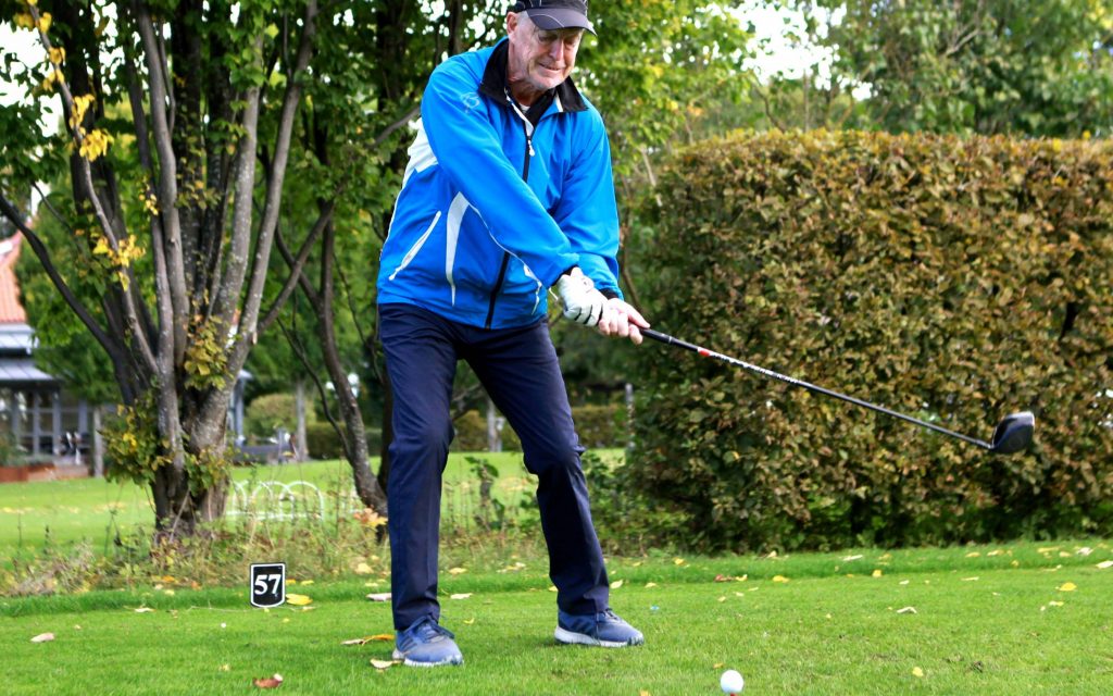 Vänsterhänt senior-golfspelare svingar golfklubban hårt mot golfbollen. 