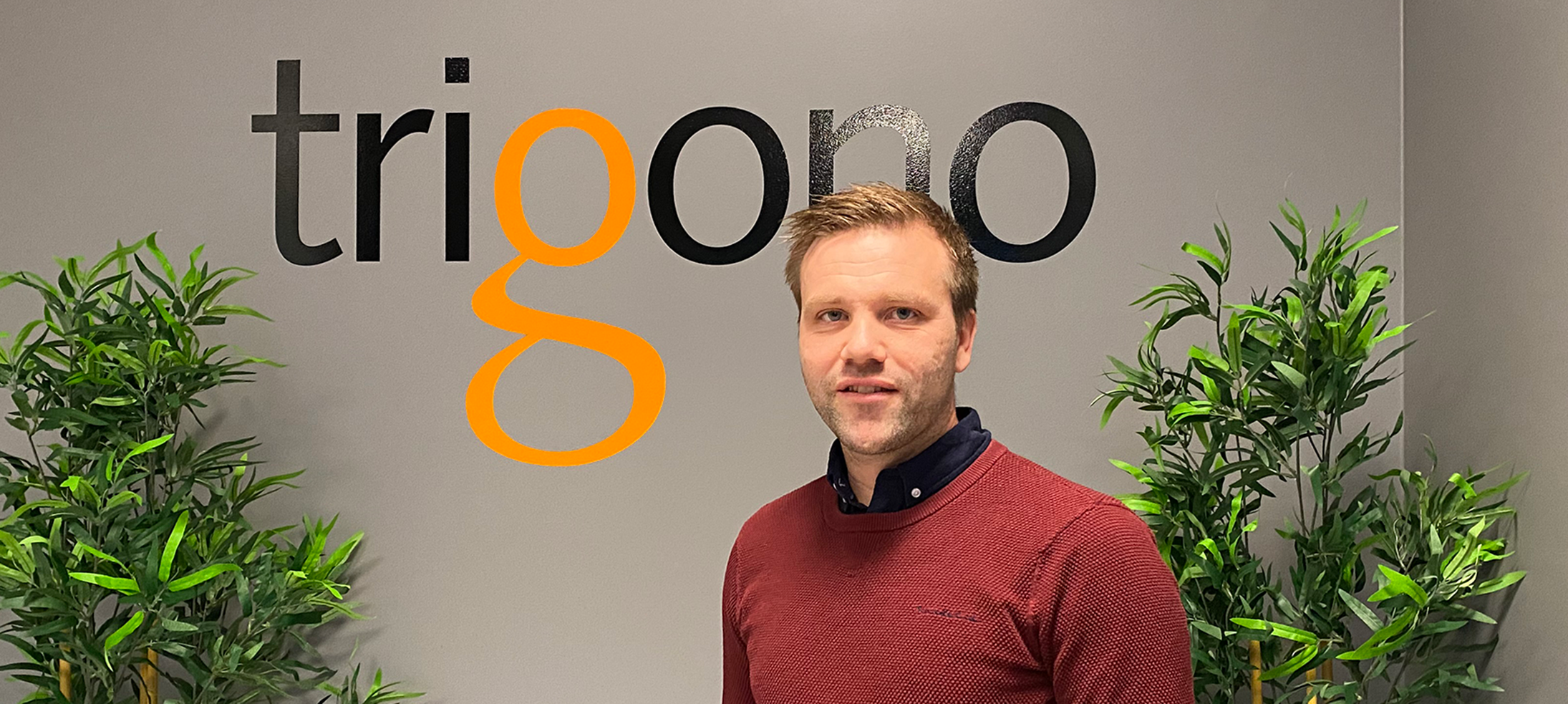 Andreas Björk som är platschef på Trigono står i företagets entré med företagsnamnet i bakgrunden.
